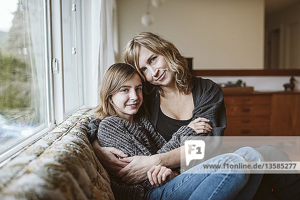 Portrait affectionate mother and daughter cuddling on living room sofa