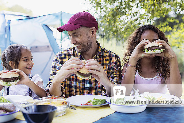 Glücklicher Vater und Töchter essen Hamburger vom Grill auf dem Campingplatz