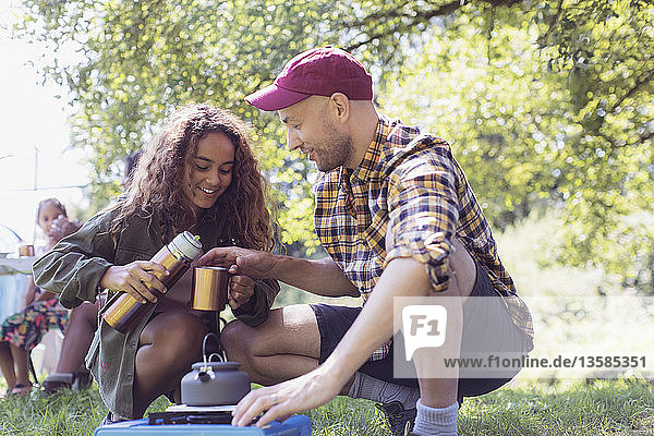 Tochter schenkt ihrem Vater am Campingkocher Kaffee aus einem isolierten Getränkebehälter ein