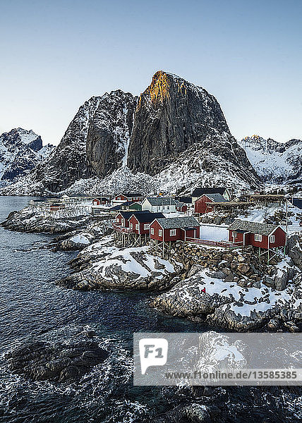 Beschauliches  schneebedecktes Fischerdorf und Klippen am Wasser  Hamnoy  Lofoten  Norwegen
