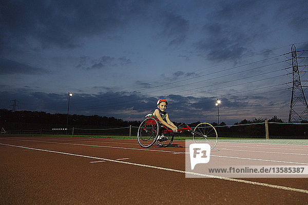 Porträt eines selbstbewussten  querschnittsgelähmten Mädchens  das auf einer nächtlichen Sportbahn für ein Rollstuhlrennen trainiert