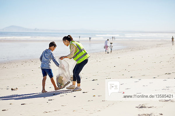 Mutter und Sohn beseitigen freiwillig Müll am sonnigen Sandstrand