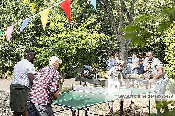 Männliche Freunde spielen Tischtennis im sonnigen Hinterhof