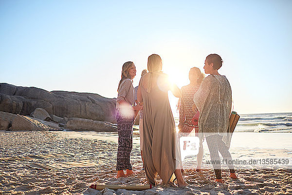 Frauen stehen im Kreis am sonnigen Strand während eines Yoga-Retreats
