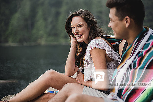 Glückliches  sorgloses junges Paar in eine Decke eingewickelt am Seeufer