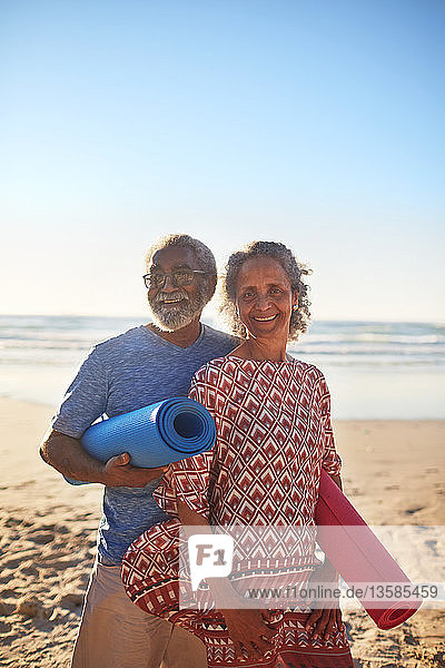 Portrait glückliches älteres Paar mit Yogamatten am sonnigen Strand