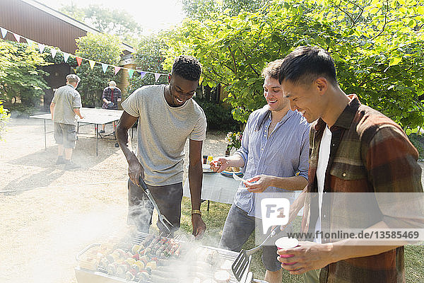 Young men barbecuing in sunny backyard