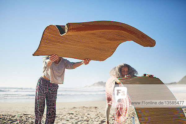 Woman laying yoga mats on sunny beach during yoga retreat