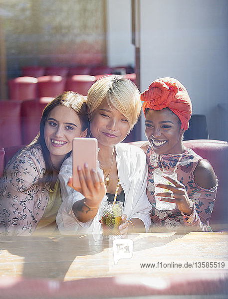 Junge Frauen Freunde trinken Cocktails und posieren für Selfie in sonnigen Restaurant