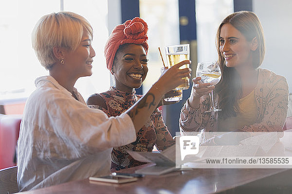 Glückliche  unbekümmerte junge Frauen stoßen in einer Bar mit einem Cocktailglas an