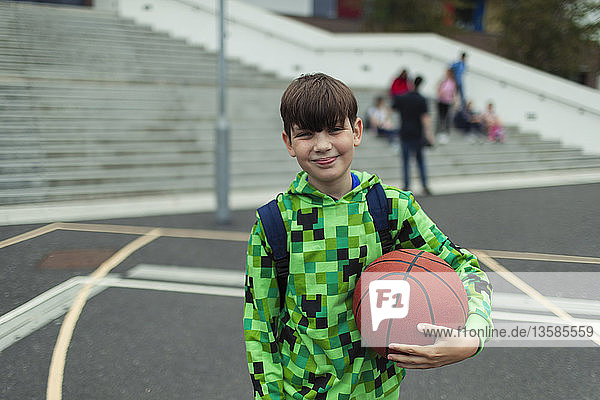 Porträt eines selbstbewussten Jungen mit Basketball auf dem Schulhof