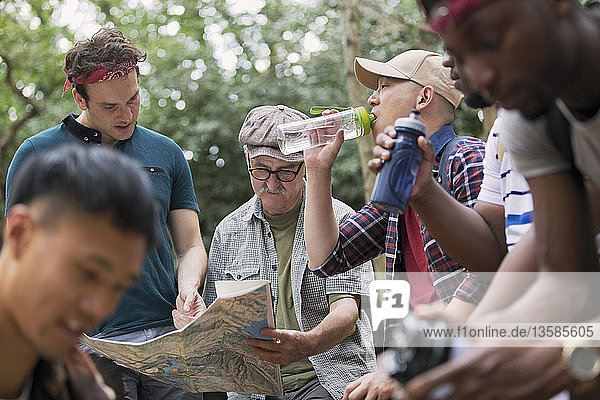 Männergruppe mit Karte und Wasserflaschen beim Wandern im Wald