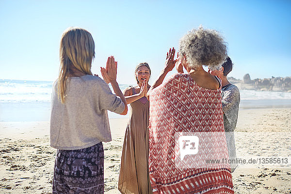 Women friends with hands clasped in circle on sunny beach during yoga retreat