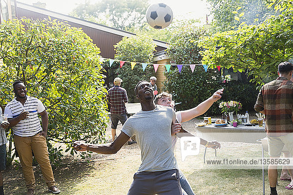 Männliche Freunde spielen Fußball und genießen ein sommerliches Grillfest im Hinterhof
