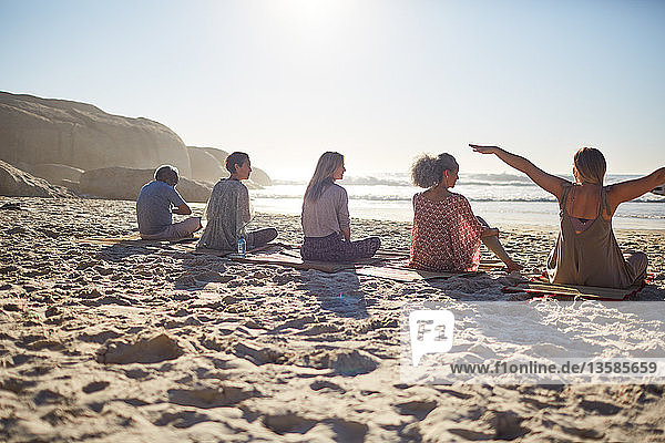 Gruppe sitzt auf Yogamatten am sonnigen Strand während eines Yoga-Retreats