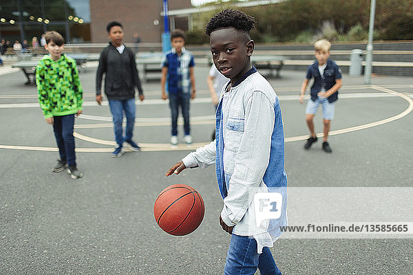 Porträt selbstbewusster kleiner Junge  der auf dem Schulhof Basketball spielt