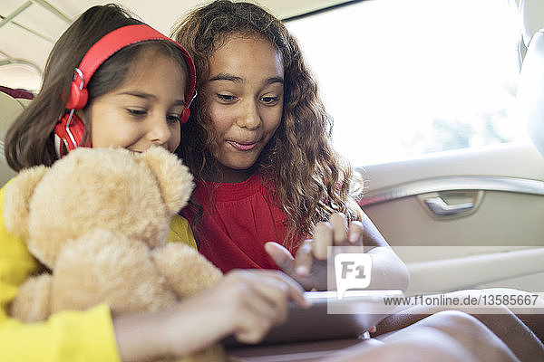 Schwestern benutzen digitales Tablet auf dem Rücksitz eines Autos