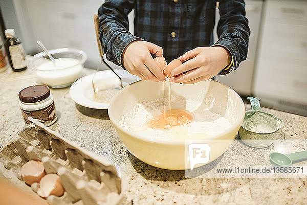 Boy baking  cracking egg into bowl in kitchen