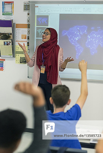 Weibliche Lehrerin im Hidschab  die vor einem Projektionsschirm im Klassenzimmer unterrichtet