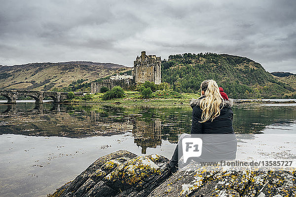 Frau genießt den Blick auf eine abgelegene Burg am Wasser  Schottland