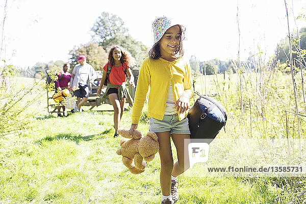 Girl camping with family  carrying sleeping bag and teddy bear
