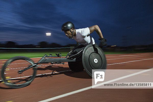 Entschlossener junger querschnittsgelähmter Sportler  der bei einem nächtlichen Rollstuhlrennen über eine Sportstrecke rast