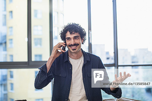 Lächelnder Mann  der in einer städtischen Wohnung mit seinem Smartphone telefoniert