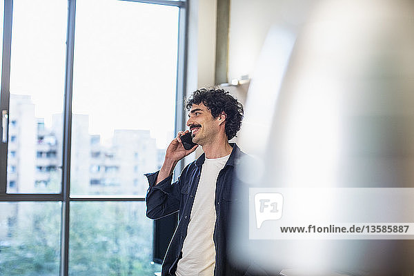 Smiling man talking on smart phone at urban apartment window