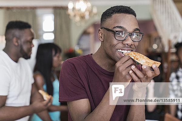 Porträt eines lächelnden Teenagers  der mit seiner Familie Pizza isst