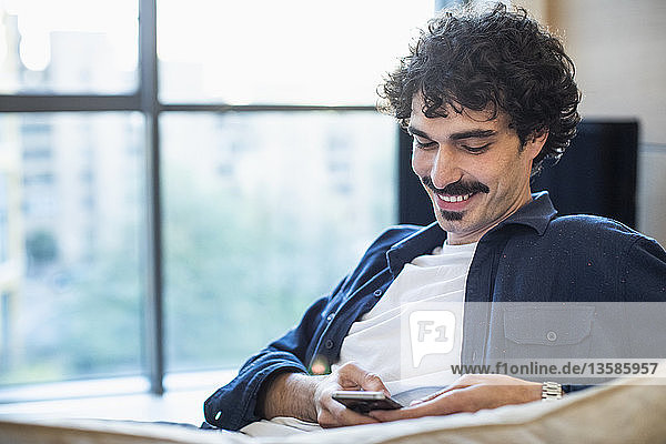 Smiling man using smart phone on sofa