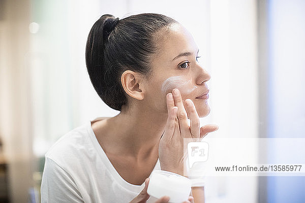 Frau trägt im Badezimmerspiegel Feuchtigkeitscreme auf das Gesicht auf