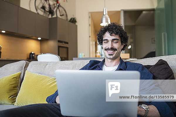 Lächelnder Mann mit Laptop auf dem Sofa einer Wohnung
