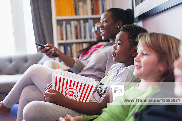 Family and friends watching movie and eating popcorn on living room sofa