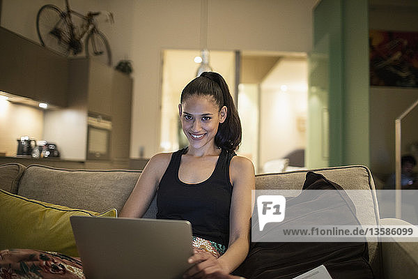 Portrait smiling woman using laptop on apartment sofa
