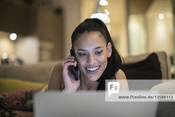 Smiling woman talking on smart phone at laptop on sofa