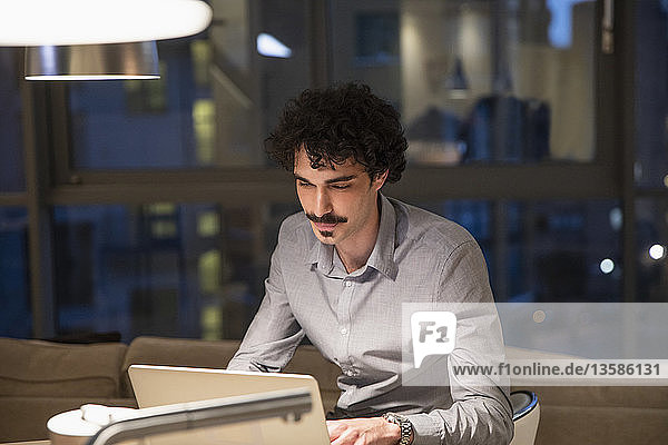 Focused man working at laptop in urban apartment at night
