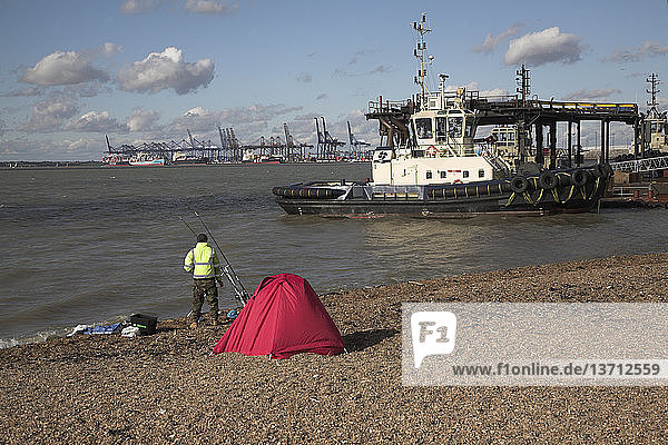 Mann mit rotem Zelt beim Angeln am Strand des Flusses Orwell neben dem Hafen von Felixstowe