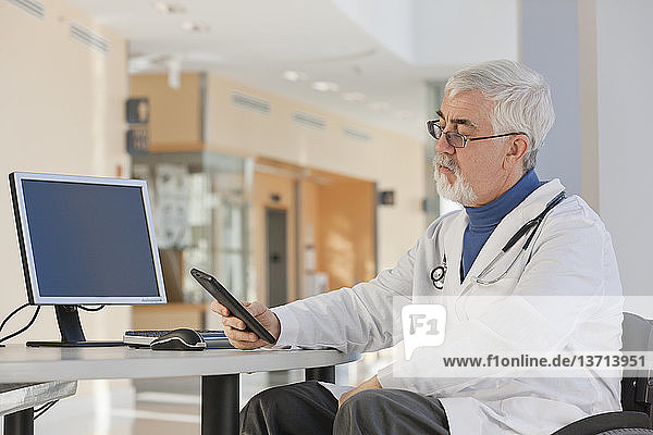 Doctor with muscular dystrophy in wheelchair looking at his tablet