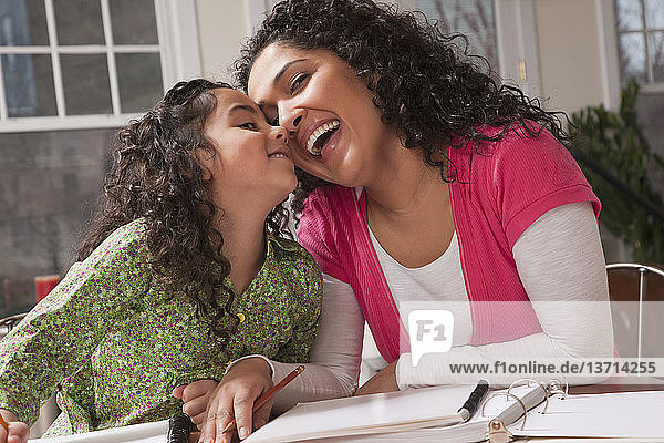 Hispanische Frau  die mit ihrer Tochter lacht  während sie Hausaufgaben macht
