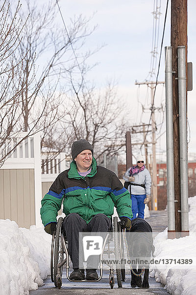 Frau mit Multipler Sklerose im Rollstuhl mit einem Diensthund im Winterschnee