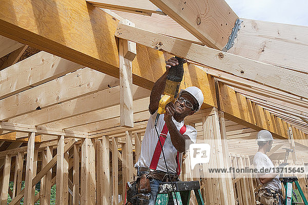 Zimmermann bei der Arbeit mit einer Säge an den Dachbrettern eines im Bau befindlichen Hauses