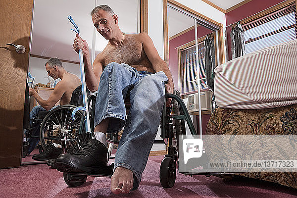 Mann mit Rückenmarksverletzung bindet seine Schuhe mit einem Verlängerungswerkzeug auf