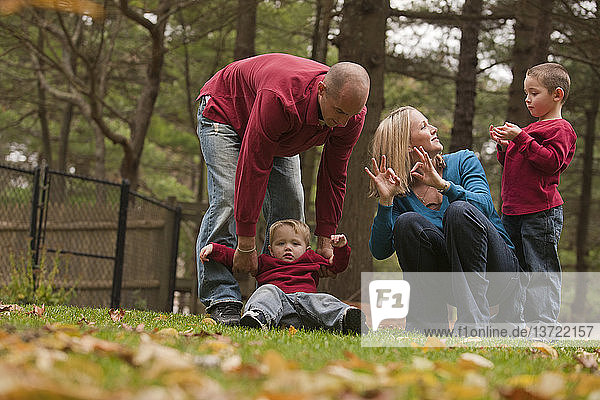 Frau  die das Wort ´Family´ in amerikanischer Zeichensprache gebärdet  während sie mit ihrer Familie in einem Park spielt
