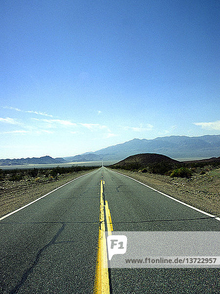 Yellow lines in straight road crossing Mojave desert between Baker and Death Valley  California  USA