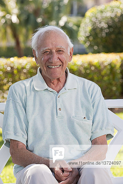 Porträt eines älteren Mannes  der auf einer Parkbank sitzt und lächelt