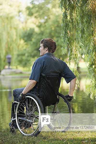 Mann mit Rückenmarksverletzung im Rollstuhl genießt den Teich in einem öffentlichen Park
