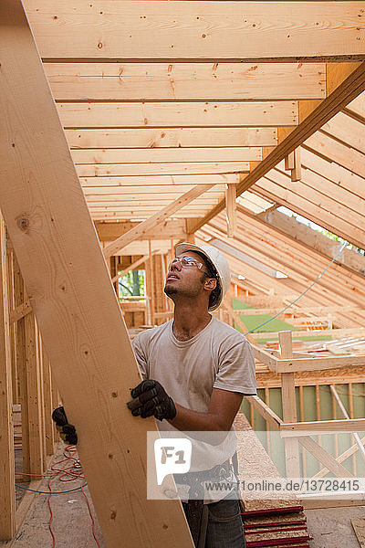 Hispanischer Zimmermann  der einen Sparren zum Dach eines im Bau befindlichen Hauses hochführt