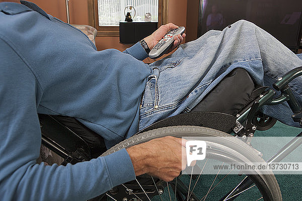 Mann mit Rückenmarksverletzung im Rollstuhl  der eine Fernsteuerung benutzt