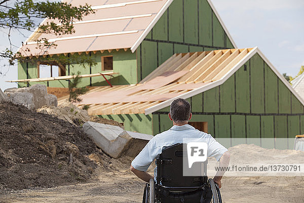 Mann mit Querschnittslähmung im Rollstuhl betrachtet sein neues  barrierefreies Haus  das gerade gebaut wird