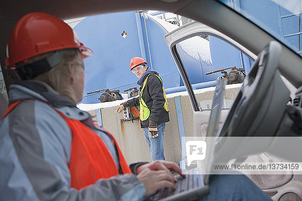 Ingenieur mit Laptop im Lkw mit einem anderen Ingenieur  der die Baustelle inspiziert